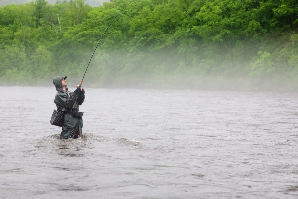 рыбак ловит рыбу на реке в дождь