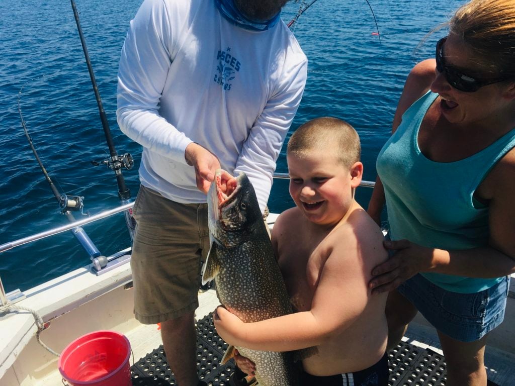 a smiling boy angler holding a fish while standing next to his parents. Fishing is a great guilt-free activity for celebrating birthdays during the pandemic