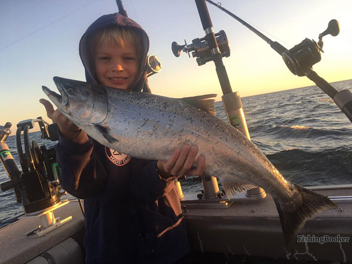 A young boy holding a Salmon which he caught on his family fishing trip in Grand Haven