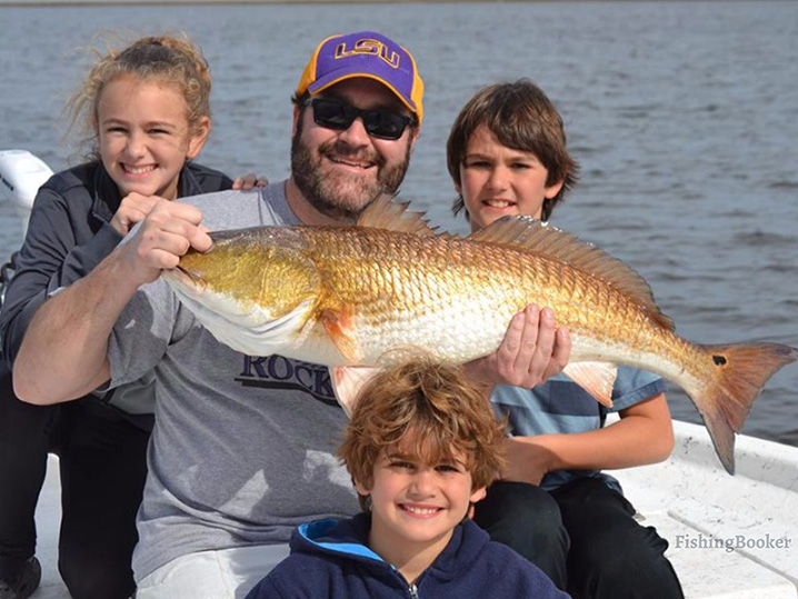 A dad and his three kids holding bull Redfish they caught on their family fishing trip in Grand Isle.