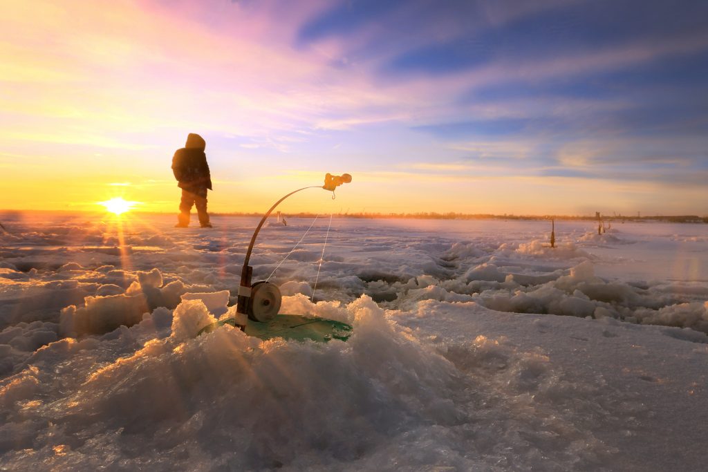 Ice fishing holes at sunset with an angler standing next to them.