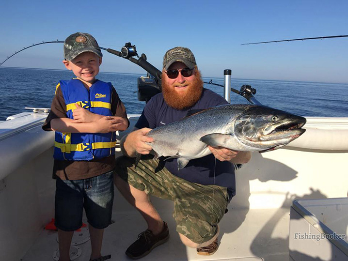 A dad and his son fishing on Lake Michigan and holding a big salmon.
