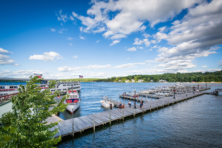 Pier on the Lake Winnipesaukee, and fishing boats around it, with trees in the background