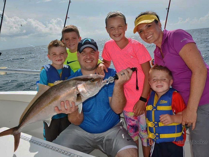 Parents and four kids on a family fishing charter in Myrtle Beach, holding an Amberjack.
