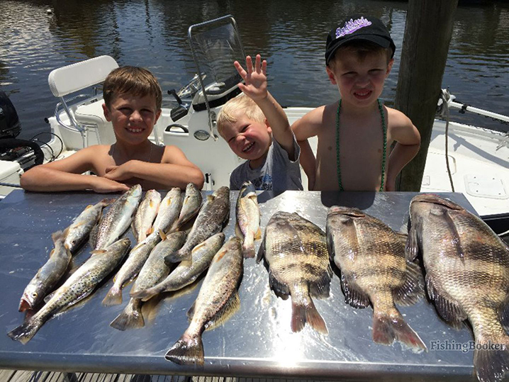 Trzech młodych chłopców robi sobie zdjęcie z pstrągami Speckled Trout i Black Drum, które złowili podczas swojej wyprawy wędkarskiej w Nowym Orleanie.