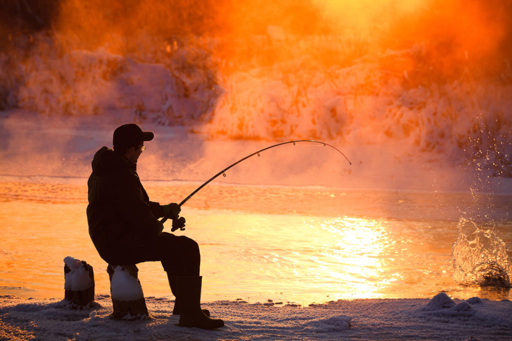 An angler fishing on an unfrozen lake in winter
