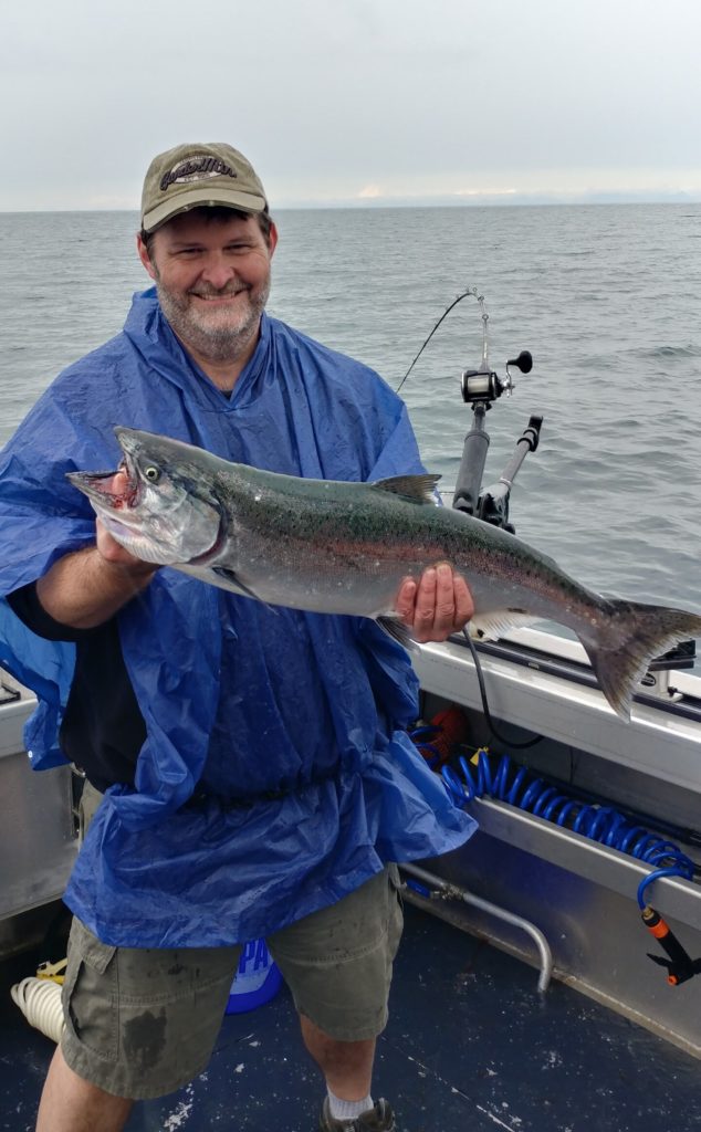 smiling angler holding a Salmon on a fishing charter in Alaska, showing that fishing is a great guilt-free activity to enjoy during the covid pandemic