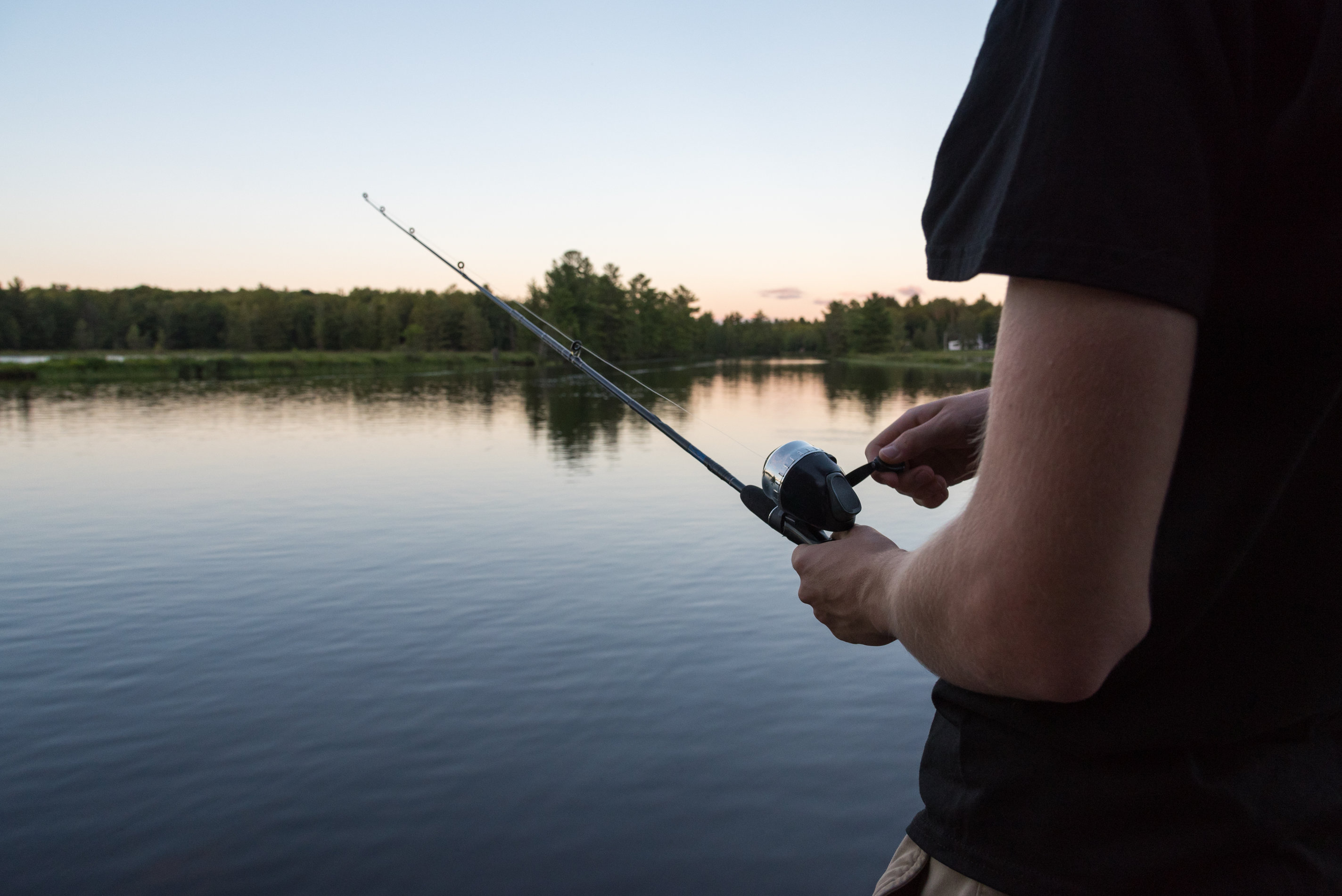 an angler holding a rod with his hand on the spincast fishing reel, and a river in the background