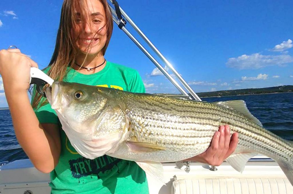 a smiling angler holding a striped bass on a boat