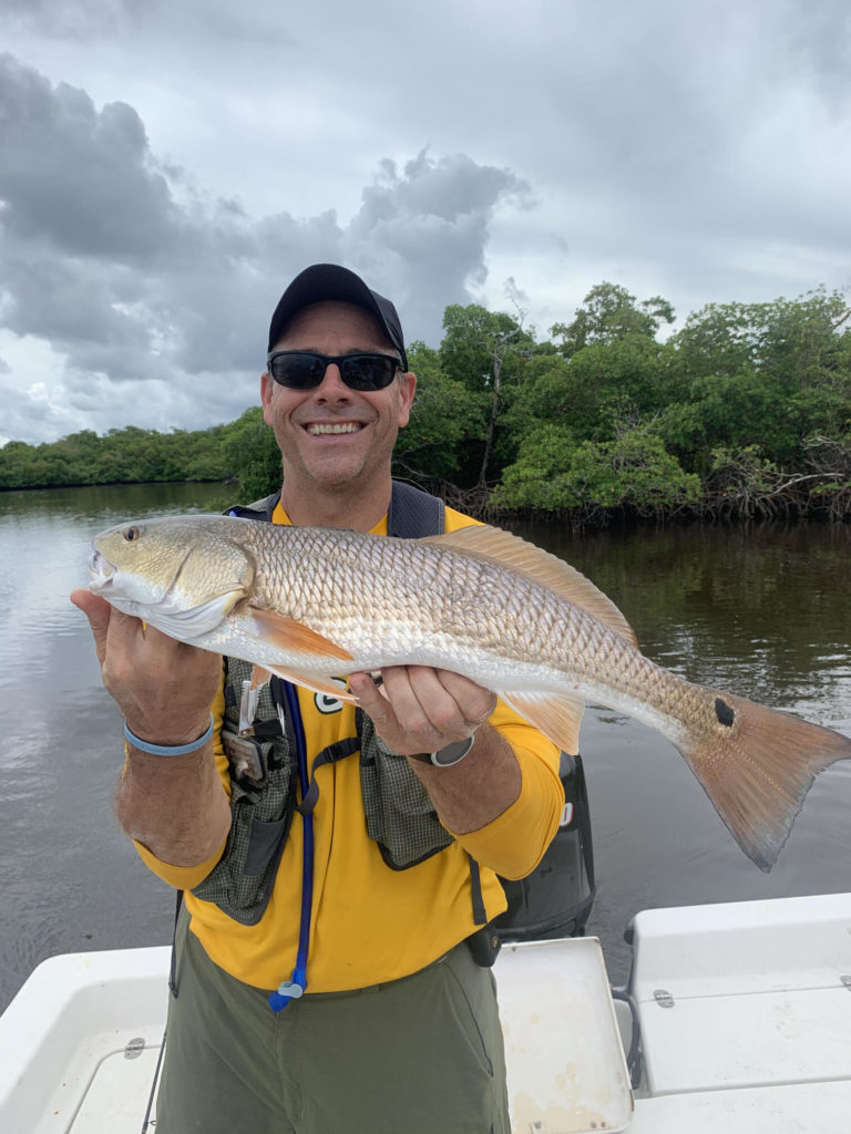 an angler posing with a Redfish on a fishing boat in the Everglades, showing that fishing is a good guilt-free activity to enjoy during the covid pandemic
