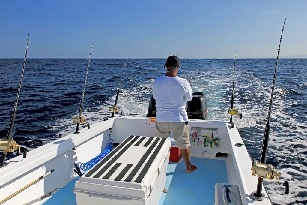 An angler looking out of a moving boat with trolling rods set up on the sides of the boat